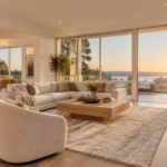 A bright, modern living room of a stylish home staged for sale, captured by a professional real estate photographer. Wide-angle lens perspective showcasing elegant interior design with warm natural light streaming through large windows, neutral beige and white tones, minimalist contemporary furniture, a tripod with a DSLR camera visible in the corner hinting at a professional shoot. High-end real estate listing photo aesthetic, soft golden hour lighting, ultra-realistic, 8K quality, architectural photography style, shallow depth of field on decorative elements.